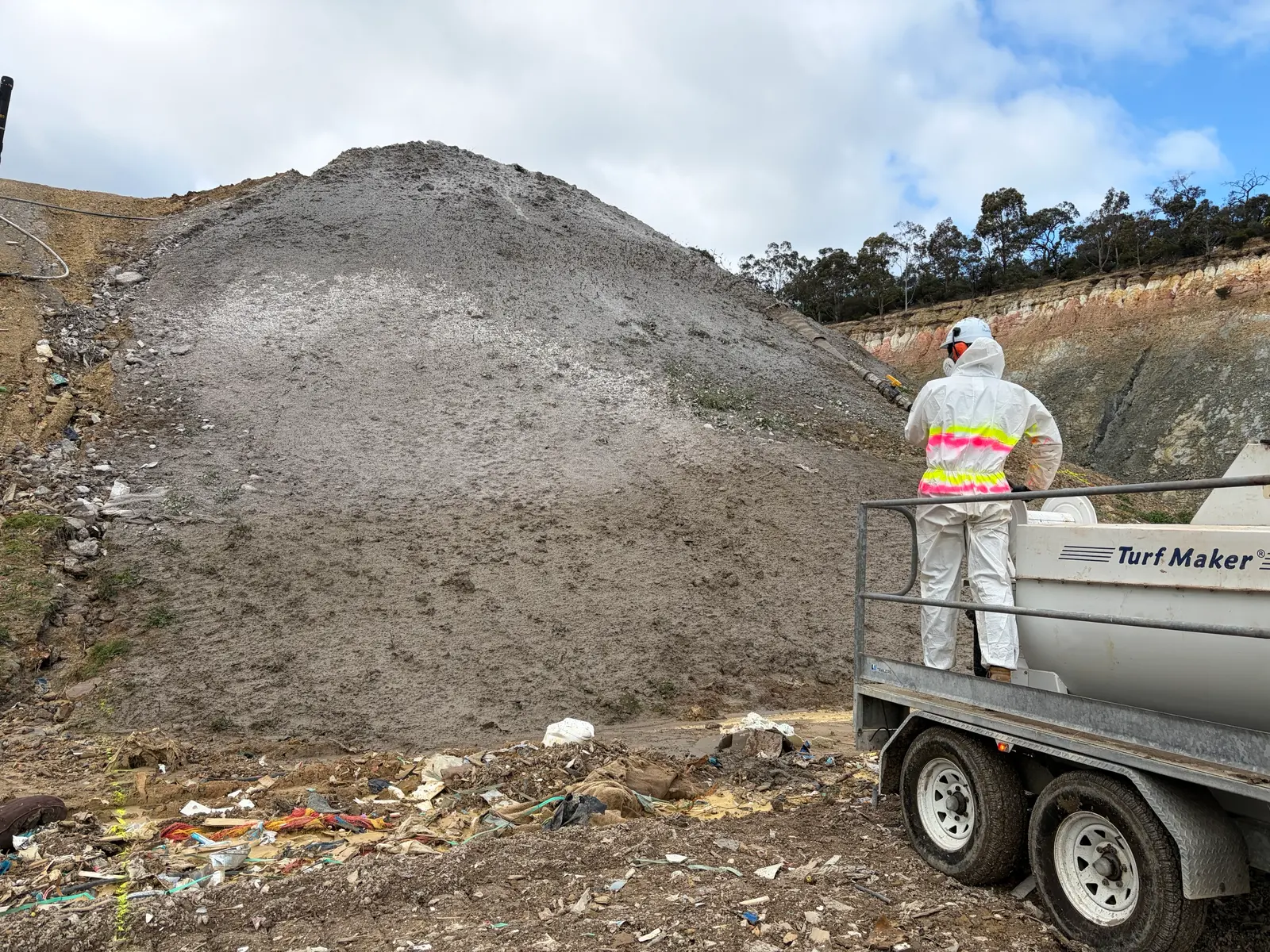 Core Environmental Projects operator in protective gear spraying Posi-Shell onto a landfill slope from a trailer-mounted applicator