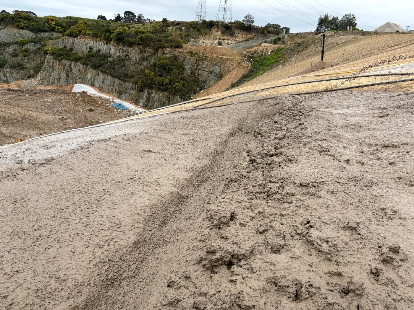 Freshly sprayed Posi-Shell coating on a landfill slope, with hoses running across the surface